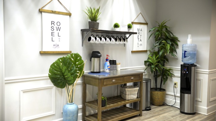 Interior beverage area with coffee maker, water cooler, potted plants, decorative signage, and wooden counter
