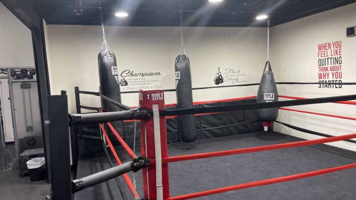 Interior recreation space with professional TITLE boxing ring, heavy punching bags, and motivational wall decals