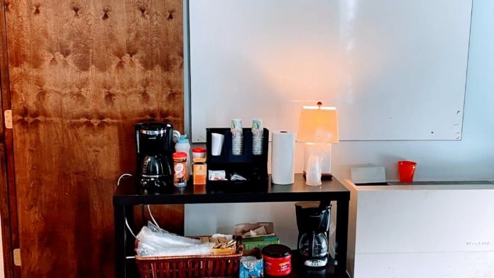 Interior break room with coffee maker, supplies, whiteboard, and table workspace