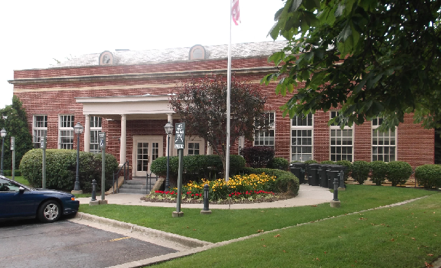 Exterior view of red brick institutional building with white entrance portico, columned entry, and landscaping