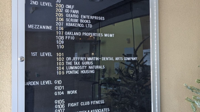 Exterior building directory sign showing suite numbers and tenant listings on tan-colored building wall