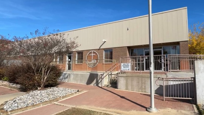 Exterior side entrance showing brick building, covered shelter area, landscaping, and ramp access