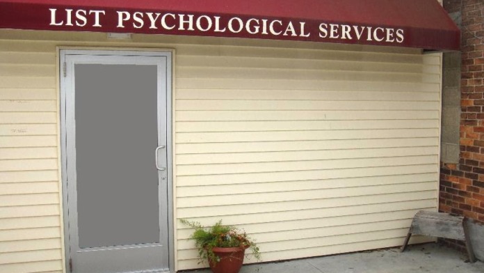 Exterior entrance to facility showing cream-colored siding, red awning with facility name, glass door, and landscaping