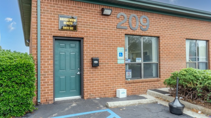 Exterior red brick building entrance showing BrightView Health Suite 102 signage, door, windows, and parking area