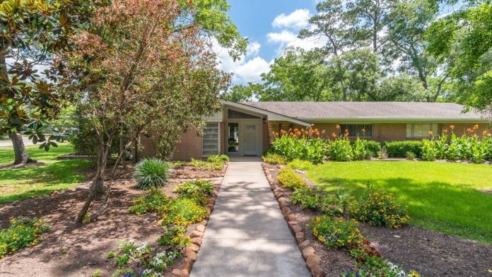 Exterior entrance pathway with red door, mature landscaping, and building facade