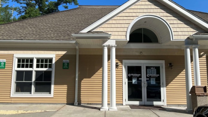 Exterior view showing facility entrance, landscaping, parking area, and directional signage
