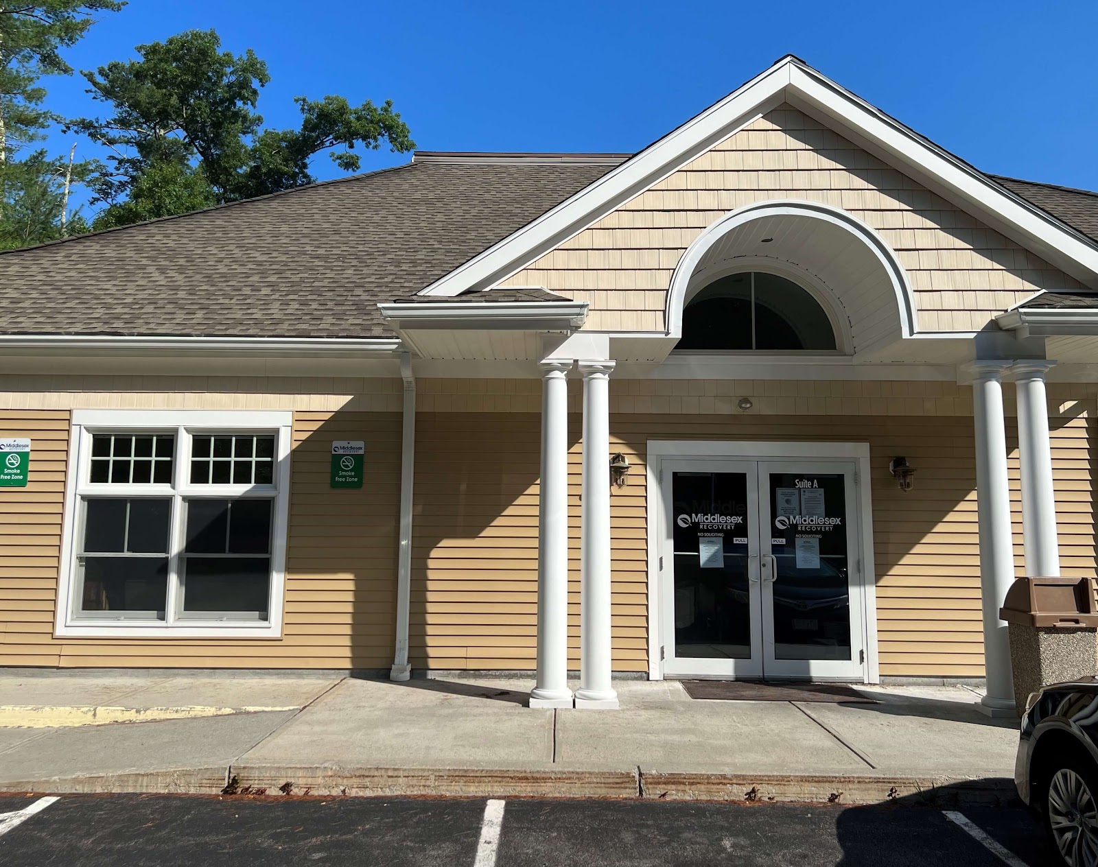 Exterior view showing facility entrance, landscaping, parking area, and directional signage