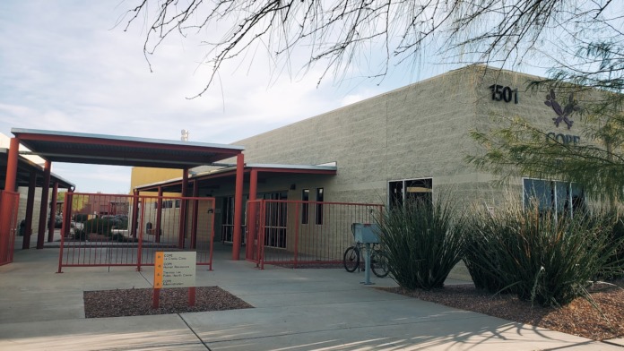 Exterior view of facility building entrance with red metal structures, concrete patio, native landscaping, and address marking 501
