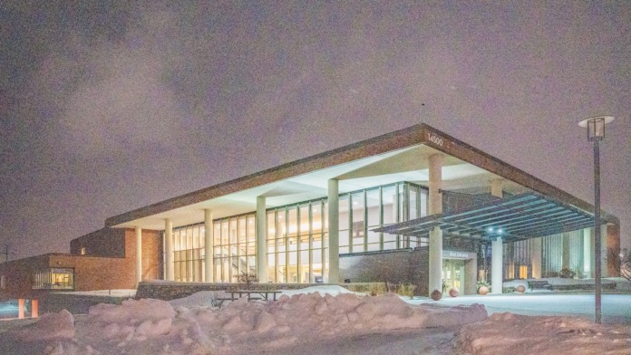Exterior evening view of facility showing brick construction, large glass windows, pergola structure, and landscaped grounds with snow