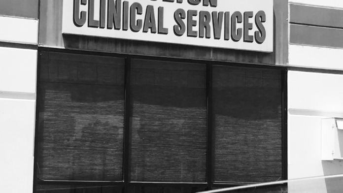 Exterior black and white image of building signage for Colton Clinical Services with shuttered windows.