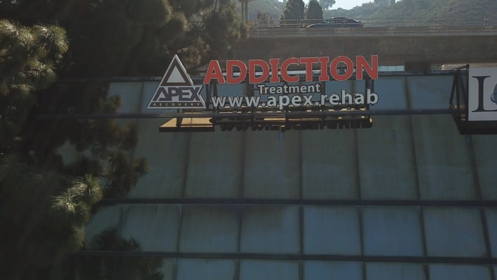 Exterior view of APEX Recovery treatment center signage on building facade with landscaping