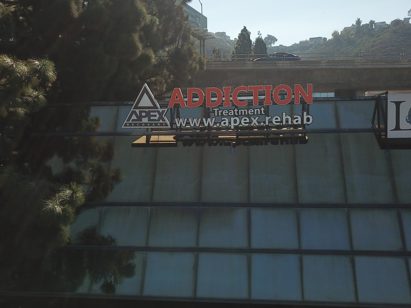 Exterior view of APEX Recovery treatment center signage on building facade with landscaping