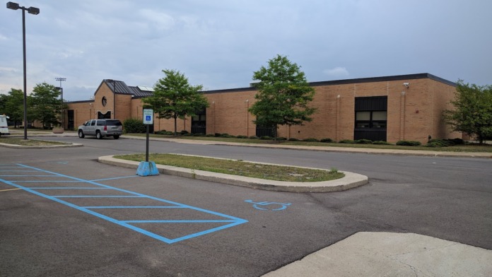 Exterior view of brick facility building with designated accessible parking spaces, concrete walkway, and landscaped grounds