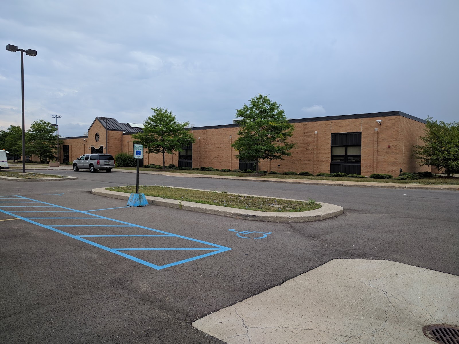 Exterior view of brick facility building with designated accessible parking spaces, concrete walkway, and landscaped grounds