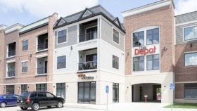 Exterior view of multi-story brick building with white trim, large windows, and ground-level entrance with parking area