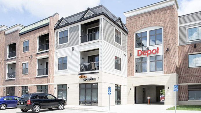 Exterior view of multi-story brick building with white trim, large windows, and ground-level entrance with parking area