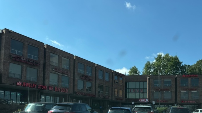 Exterior view of multi-story brick building with parked vehicles, showing facility location in shopping complex with other businesses