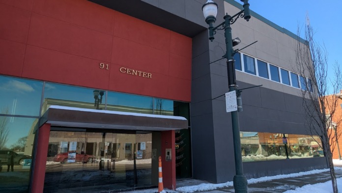 Exterior view of 91 CENTER building with red and gray paneling, glass entrance, street lamp, and snow-covered ground