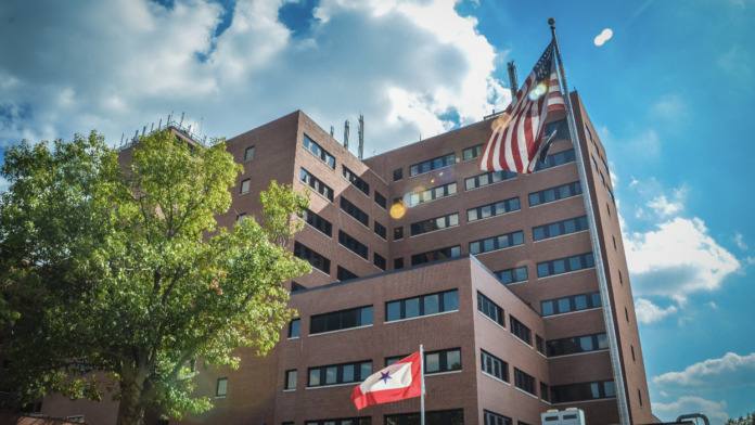 Exterior hospital building facade with flags against cloudy blue sky
