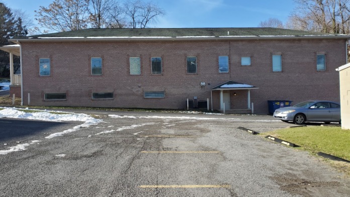 Exterior of brick facility showing side entrance with covered portico, white columns, and landscaped grounds
