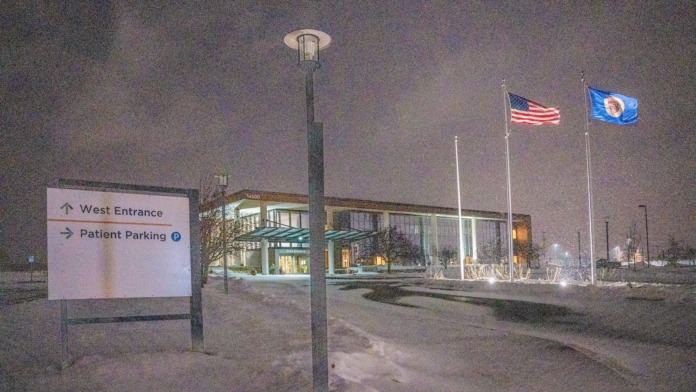 Exterior parking and entrance area with directional sign showing west entrance and patient parking, American and Minnesota flags, facility lighting