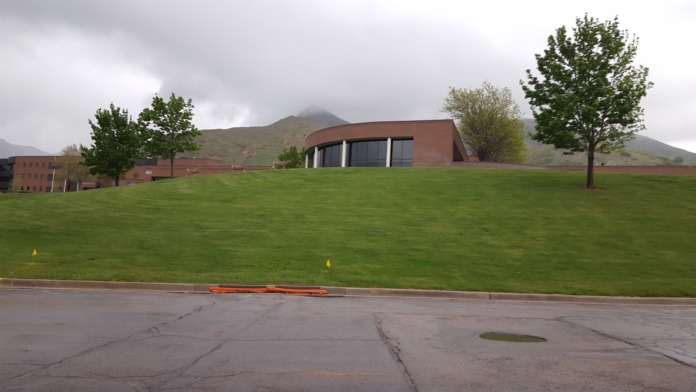 Exterior view of modern brick building with large lawn, trees, and mountain landscape background