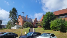 Exterior view of parking area with vehicles and brick academic buildings on sloped grounds