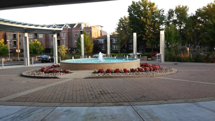 Outdoor courtyard featuring central water fountain with landscaping, red flowers, trees, and surrounding facility buildings