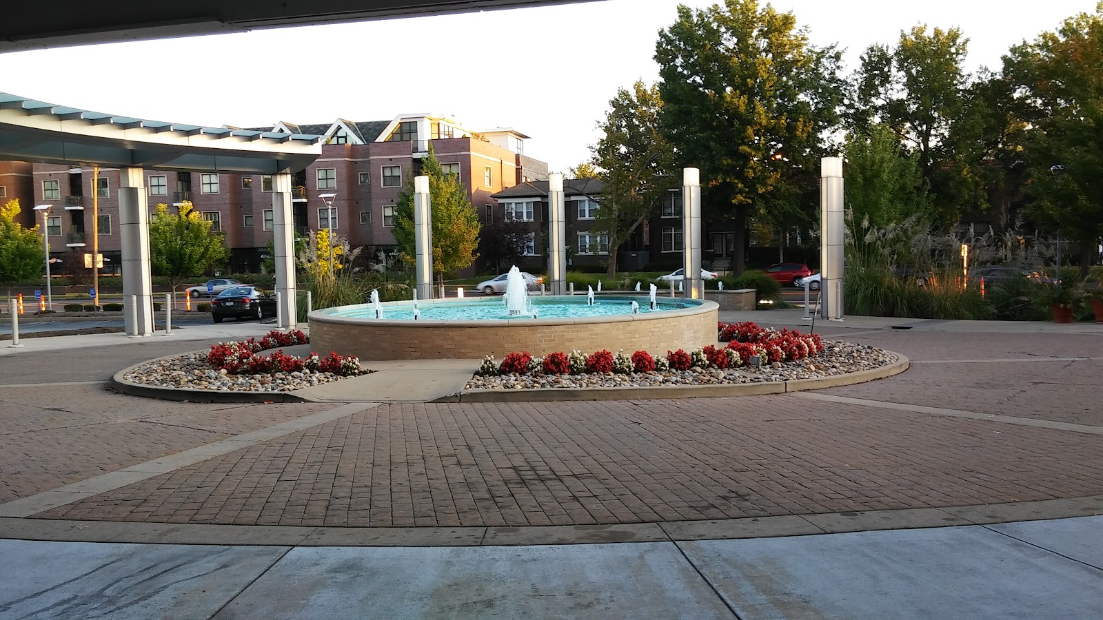Outdoor courtyard featuring central water fountain with landscaping, red flowers, trees, and surrounding facility buildings