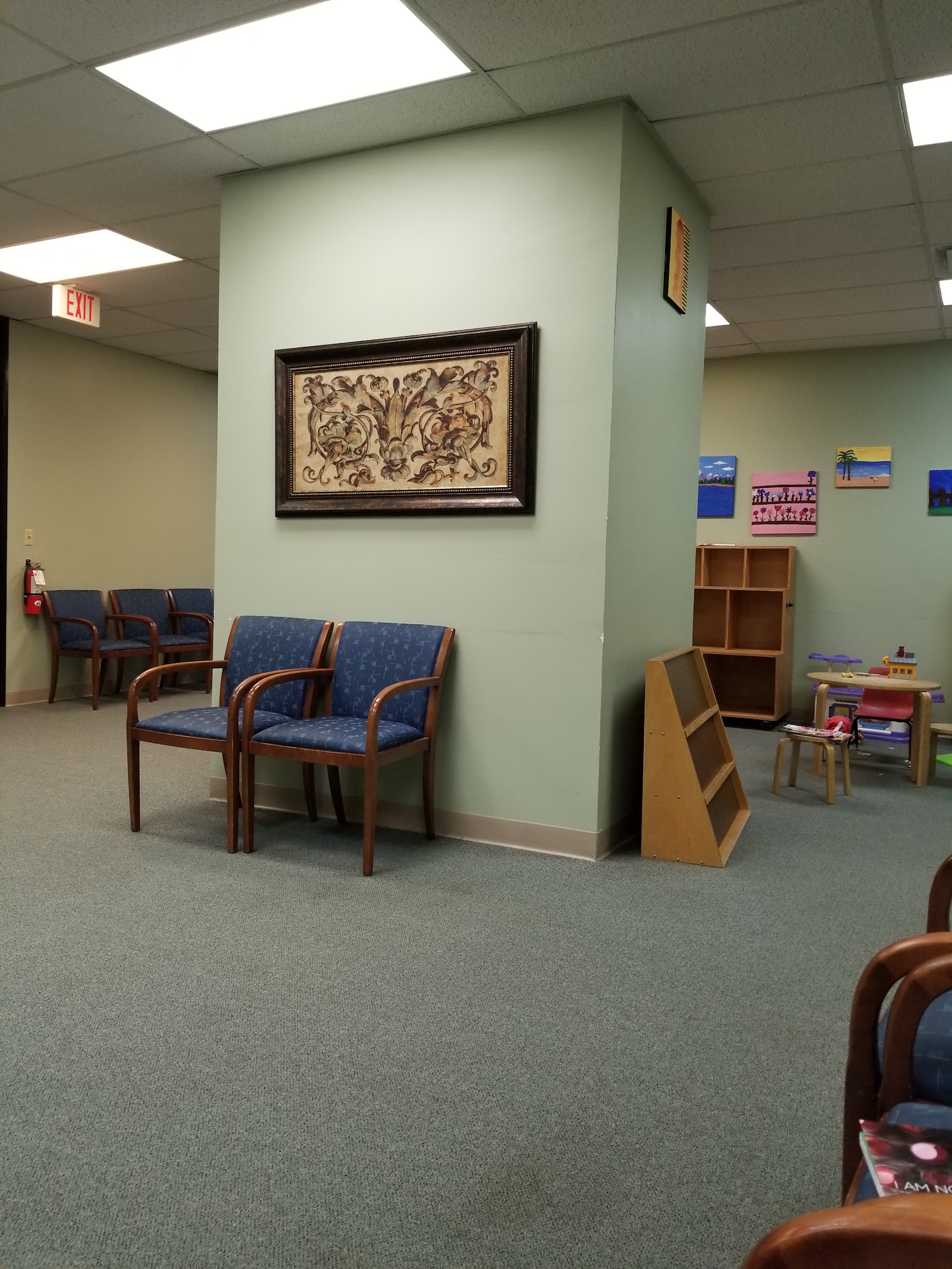 Interior play space with wooden storage units, small chairs, children's artwork gallery on green walls, and colorful decorations
