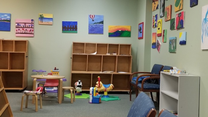 Interior playroom with educational toys, storage cubbies, colorful artwork on walls, wooden furniture, and floor play mats