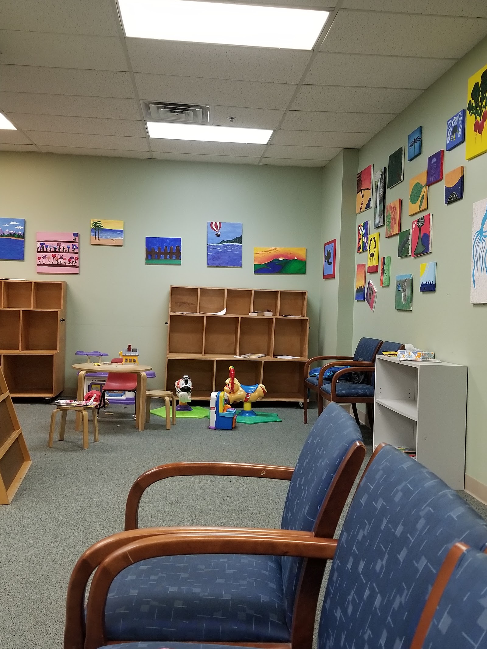 Interior playroom with educational toys, storage cubbies, colorful artwork on walls, wooden furniture, and floor play mats