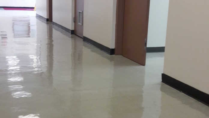 Interior hallway with white walls, brown wooden doors, recessed ceiling lights and facility informational signage