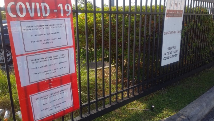 Exterior gate with red COVID-19 testing signage displaying testing schedules and bilingual information