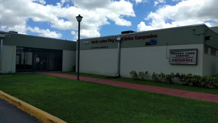 Exterior front view of clinic building with green landscaping, red awning, black perimeter fence, and clear signage