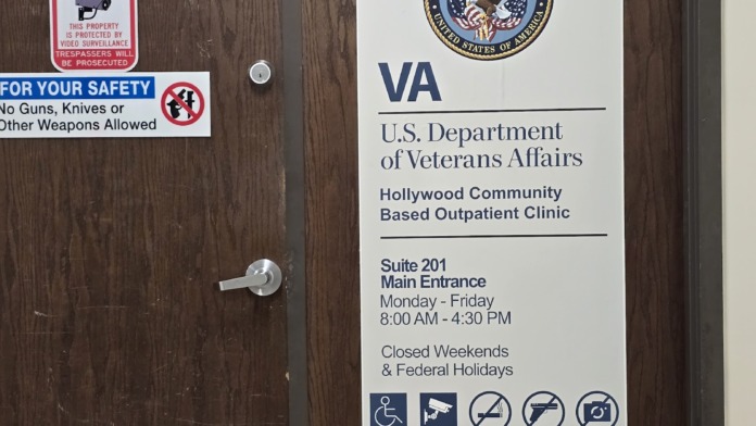Interior view of dark wooden clinic entrance door with VA Department of Veterans Affairs signage, Suite 201 designation, and operating hours