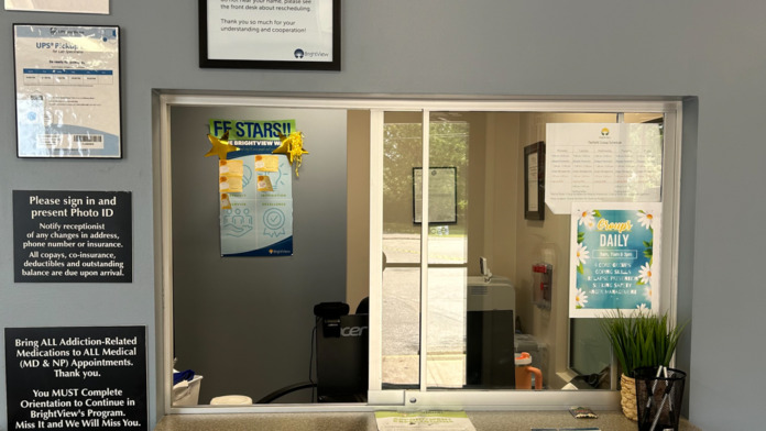 Interior reception window with gray countertop, patient materials, welcome signage, and clinic information posters displayed.