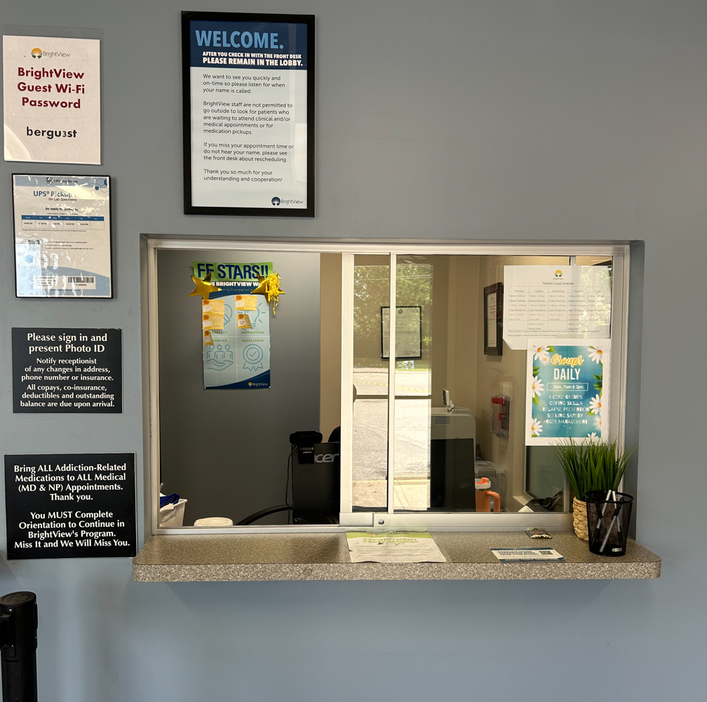 Interior reception window with gray countertop, patient materials, welcome signage, and clinic information posters displayed.