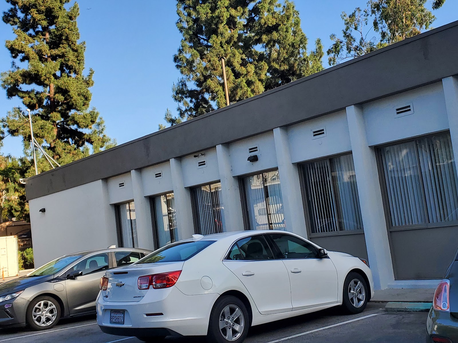 Exterior of modern white facility building with dark trim, vertical panels, windows and parked vehicles
