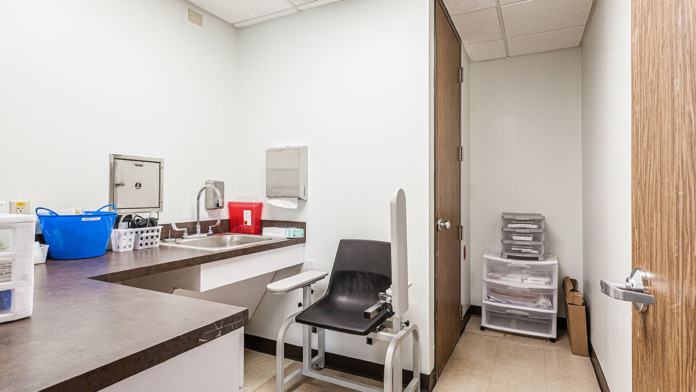 Interior treatment room with cabinetry, examination chair, medical equipment storage, and clinical workspace