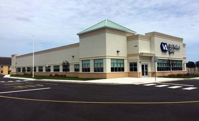 Exterior perspective of VA Outpatient Clinic showing full building structure, metal roof trim, signage, and parking area