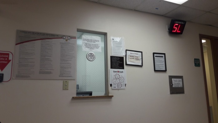 Interior hallway with white walls, brown wooden doors, recessed ceiling lights, and informational posters