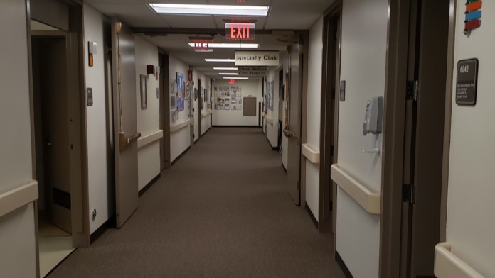 Interior corridor with multiple clinical treatment room doors, signage, and modern healthcare facility design