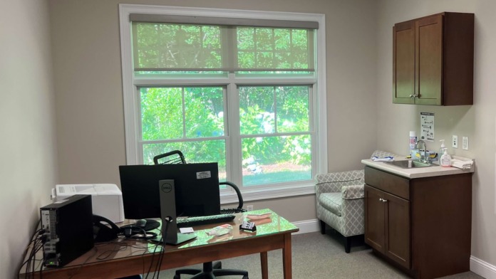 Interior office room with desk, computer monitor, windows overlooking greenery, and medical workspace