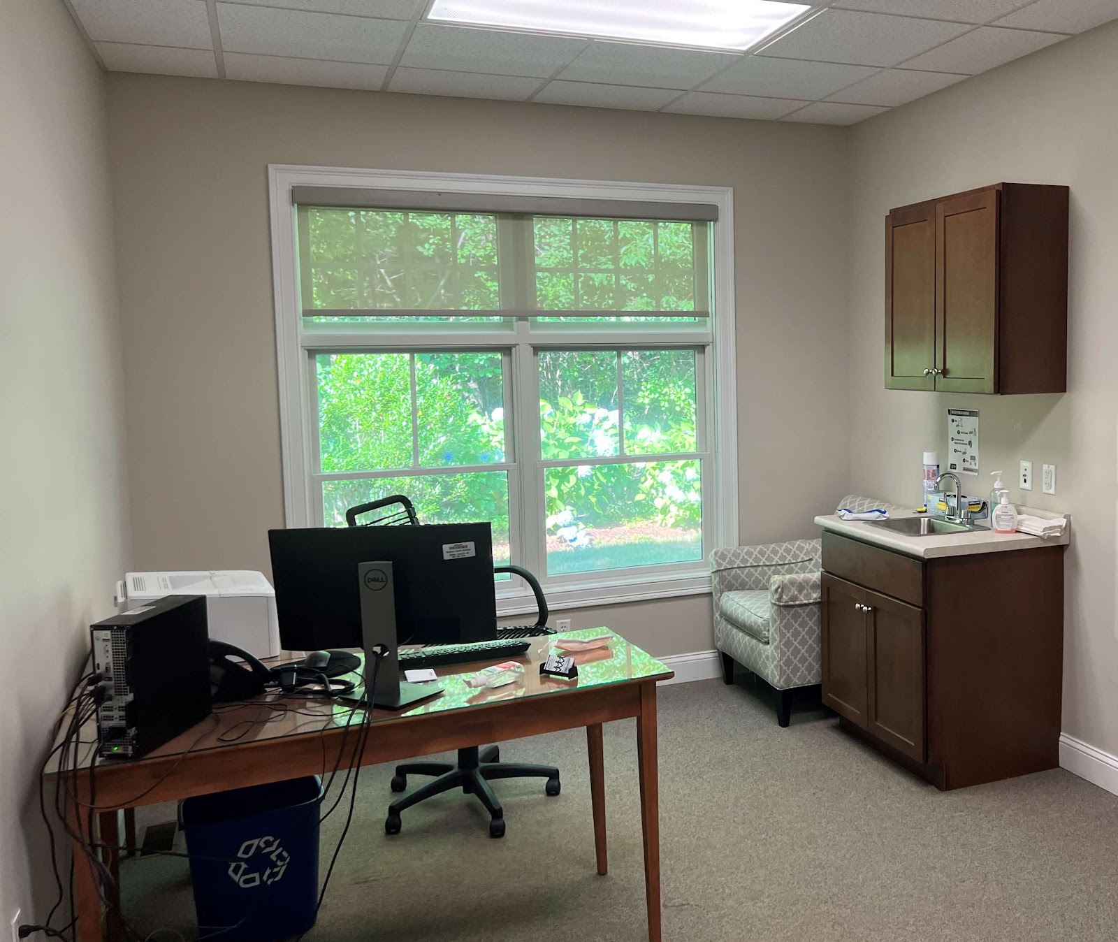 Interior office room with desk, computer monitor, windows overlooking greenery, and medical workspace