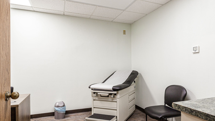 Interior examination room with treatment bed, white cabinetry, sink, and medical equipment storage