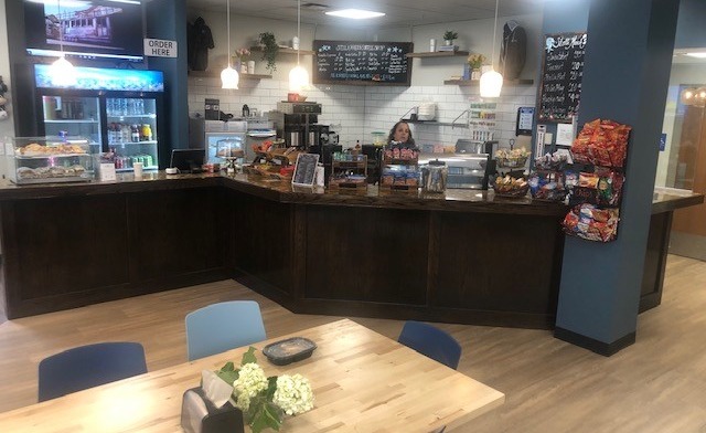 Interior coffee shop with service counter, refrigerated cases, menu board, and seating area