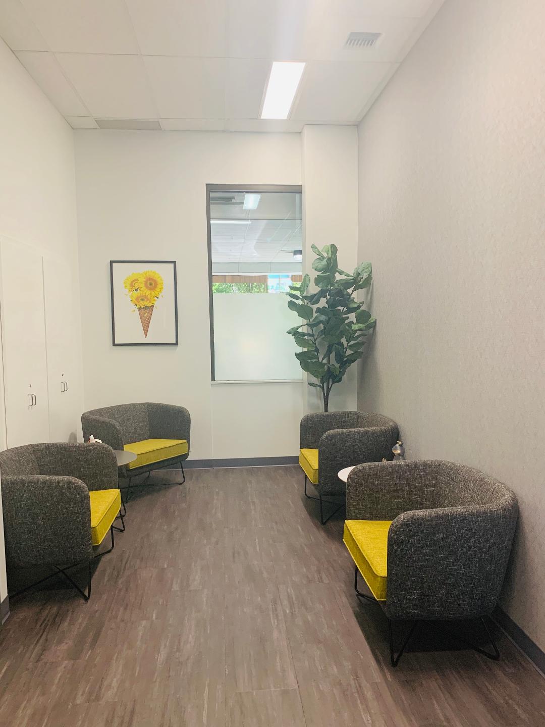 Interior lounge with gray upholstered chairs with yellow cushions, potted plant, and framed artwork on walls