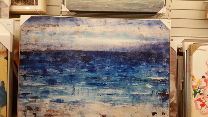 Interior wall displaying abstract seascape artwork in blues and creams, flanked by framed pieces and decorative items