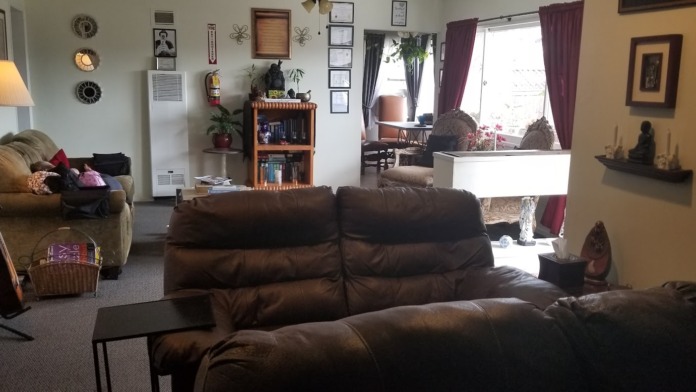 Interior common area with brown leather sectional sofa, armchair, wooden bookshelf, wall decor, and large windows with curtains